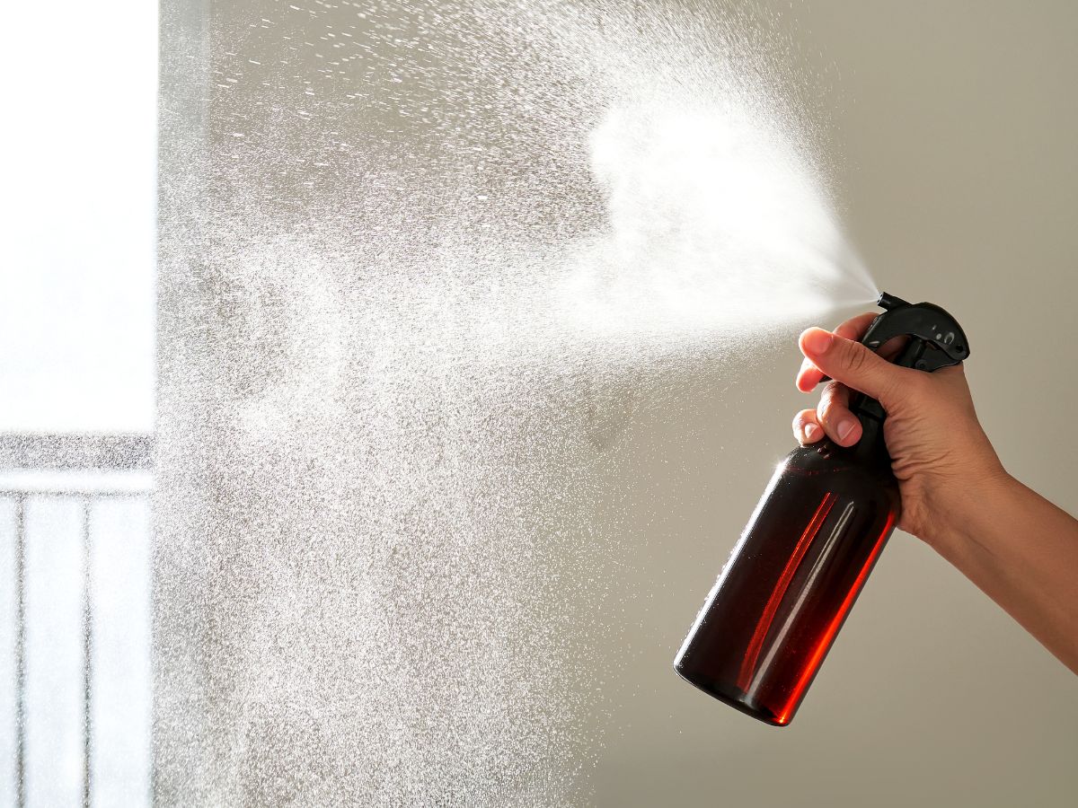 stock image of hand spraying a mist out of an amber glass bottle